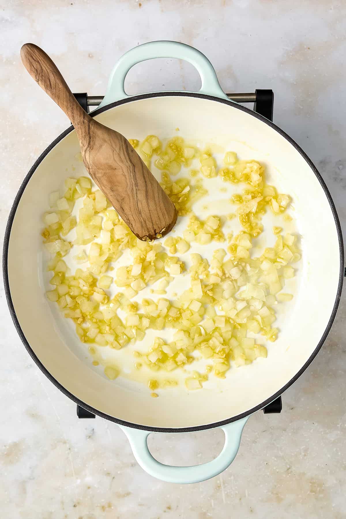 Onion cooking in olive oil in a large skillet with a wooden spoon.