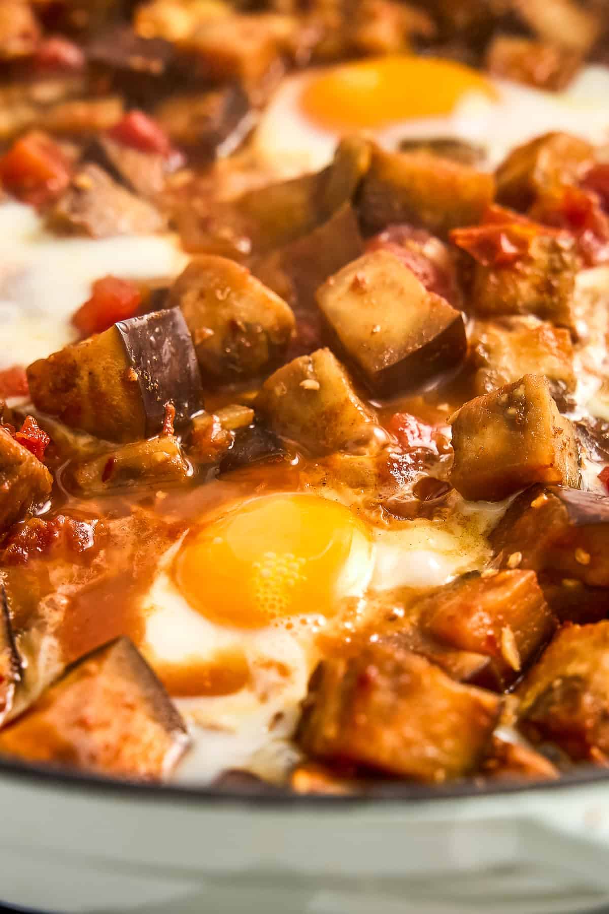 Poached eggs cooking on top of eggplant and tomato stew in a skillet.
