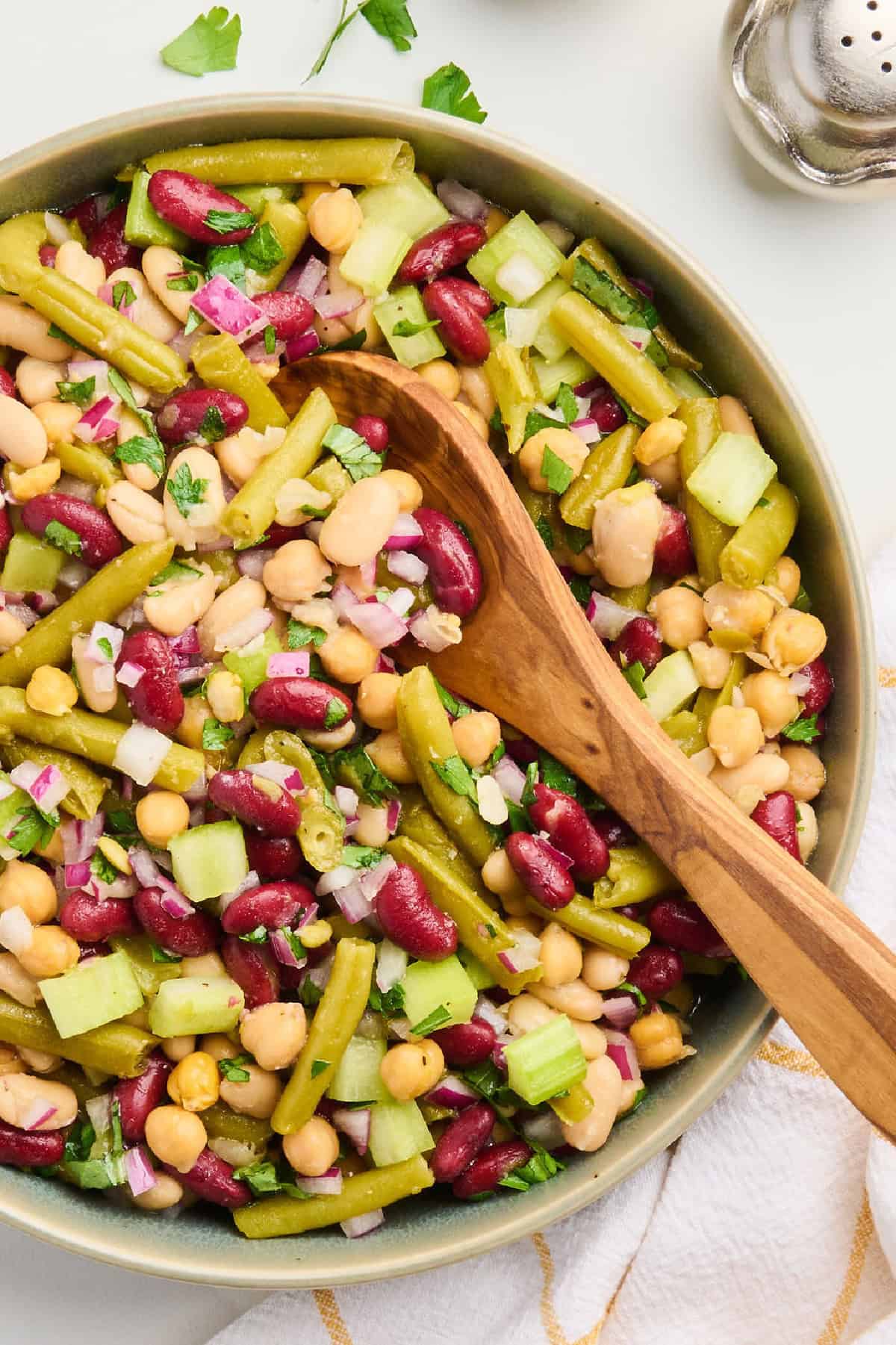 Kidney, white, green, and garbanzo bean salad in a bowl with wooden spoon.