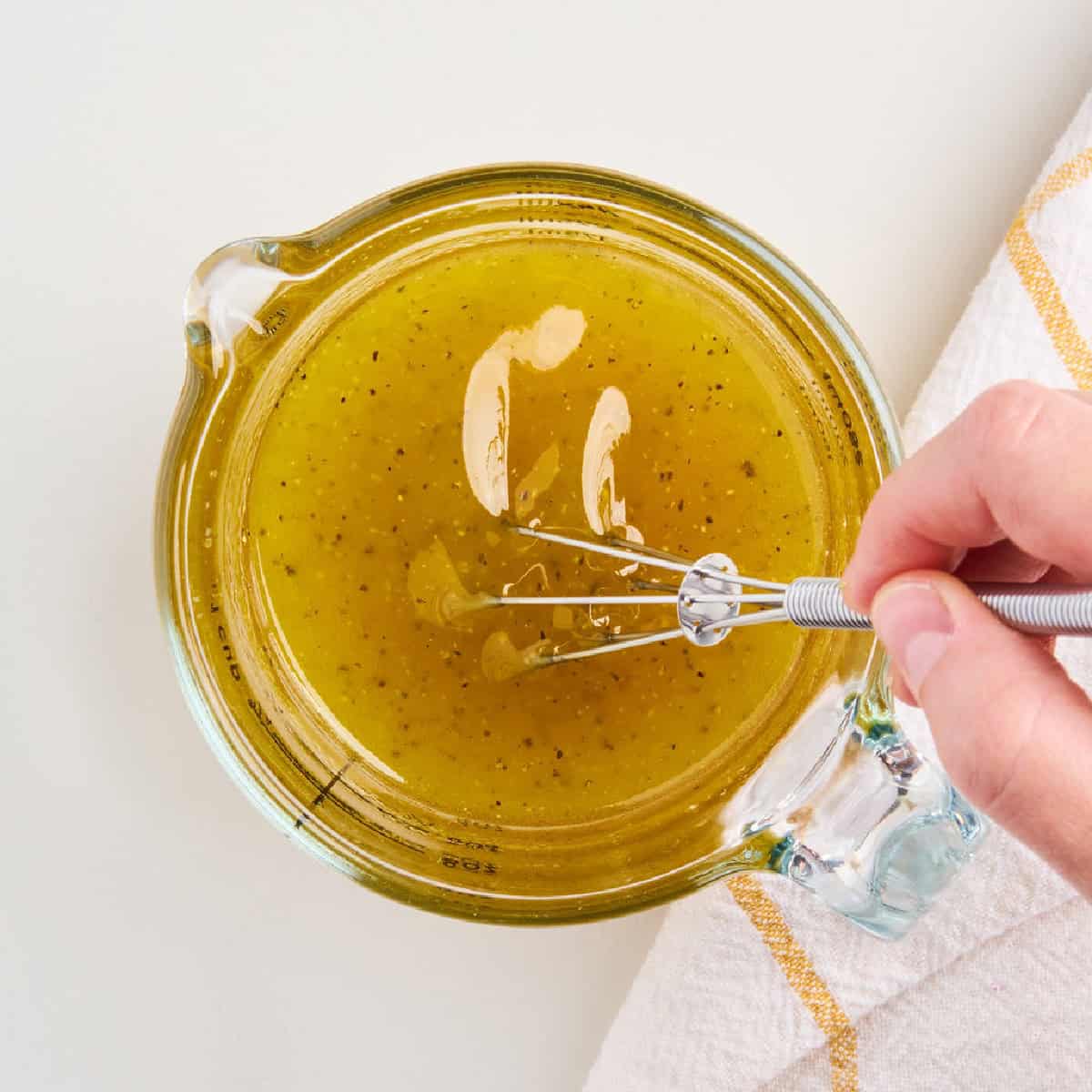 Woman whisking olive oil, honey, and apple cider vinegar together in a measuring cup.