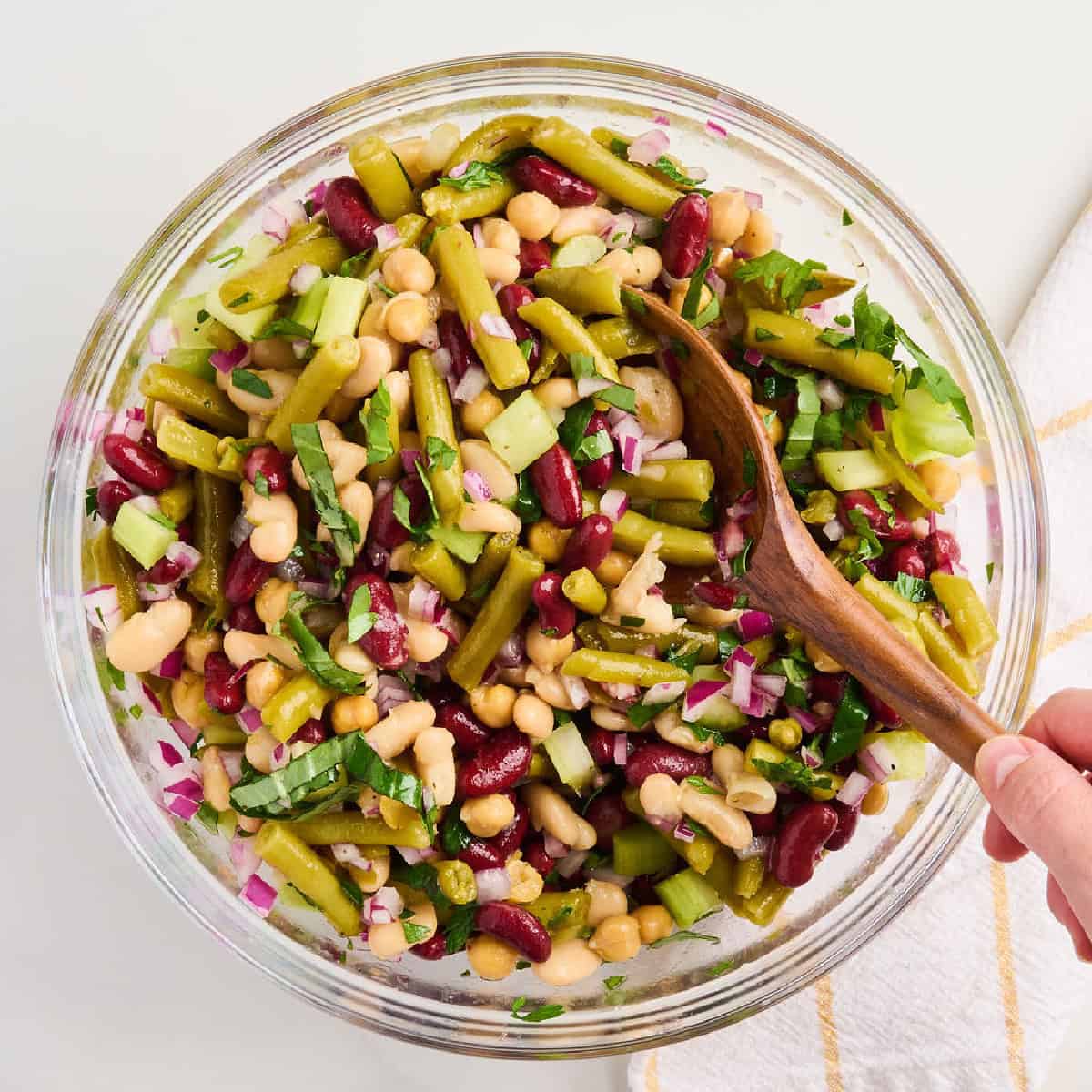 Woman stirring four bean salad ingredients with herbs and dressing until coated.