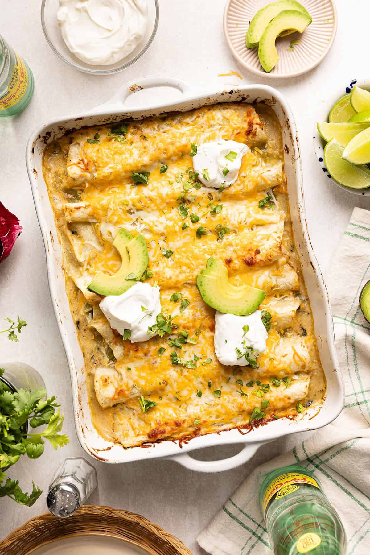 Vegetarian enchiladas recipe in a baking dish topped with avocado, sour cream, and cilantro.
