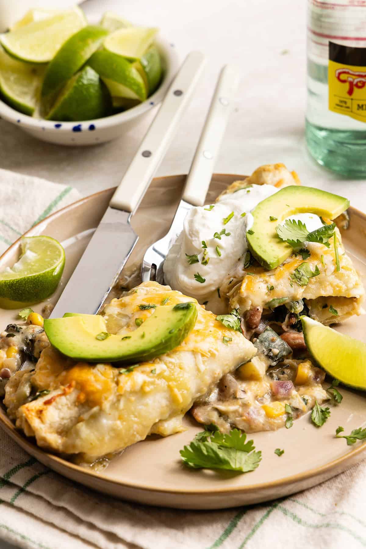 Enchilada cut in half and topped with avocado, sour cream, and cilantro on a plate.