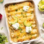 Vegetarian enchiladas recipe in a baking dish topped with avocado, sour cream, and cilantro.