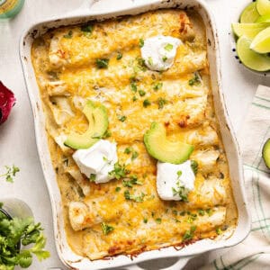 Vegetarian enchiladas recipe in a baking dish topped with avocado, sour cream, and cilantro.