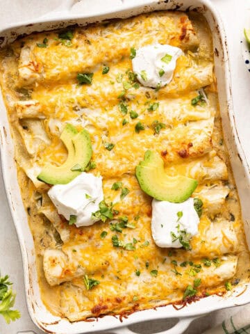 Vegetarian enchiladas recipe in a baking dish topped with avocado, sour cream, and cilantro.