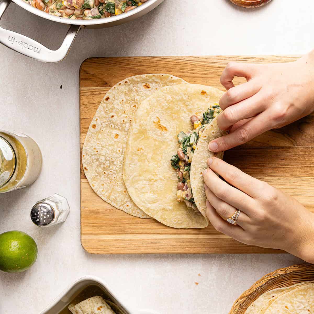 Woman rolling up a tortilla with filling to form an enchilada.