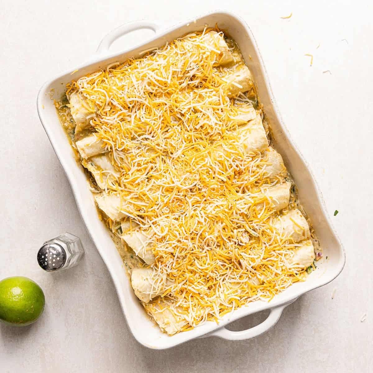 Shredded Mexican cheese sprinkled on top of a dish of enchiladas before baking.
