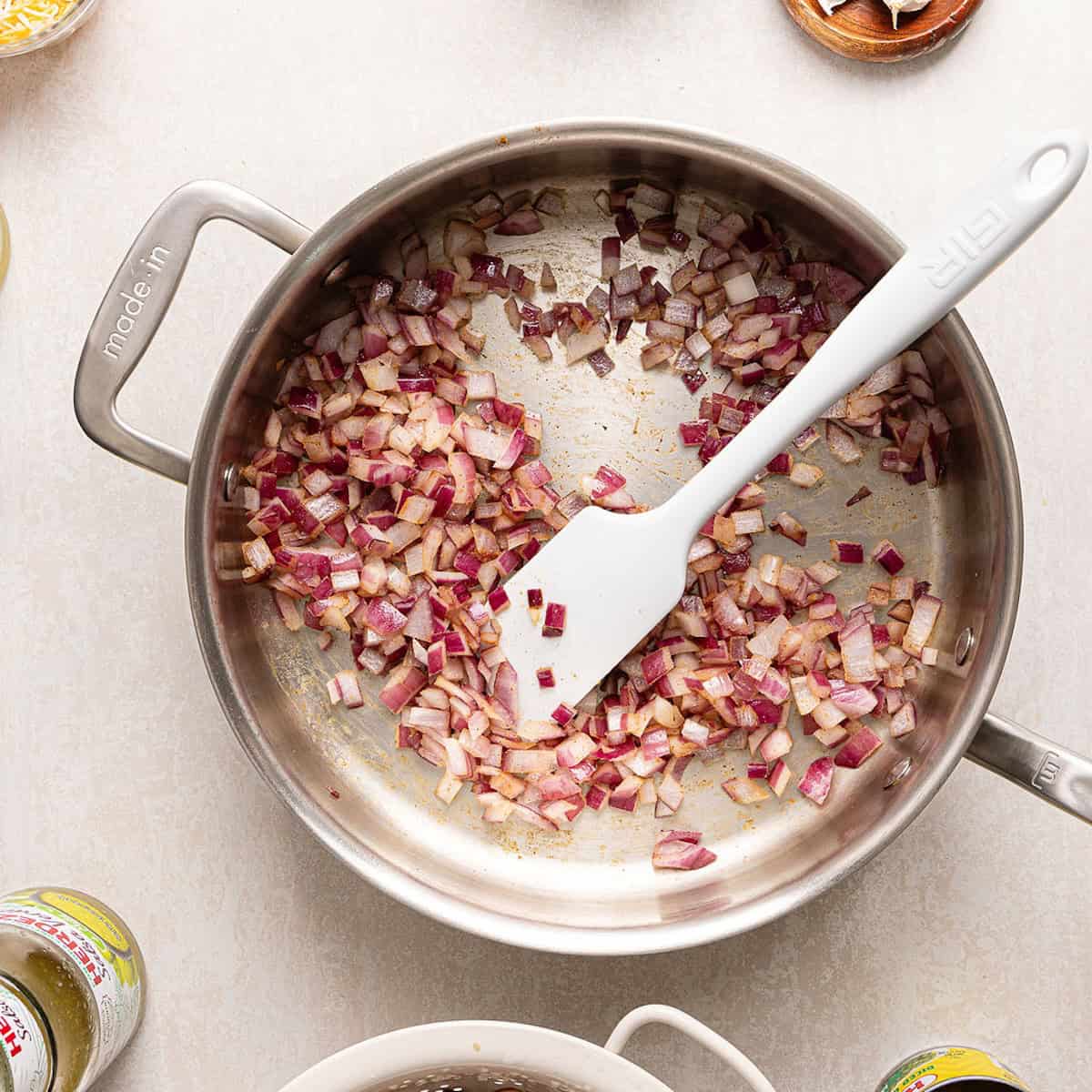 Red onion cooking in olive oil, garlic, and cumin in a skillet.