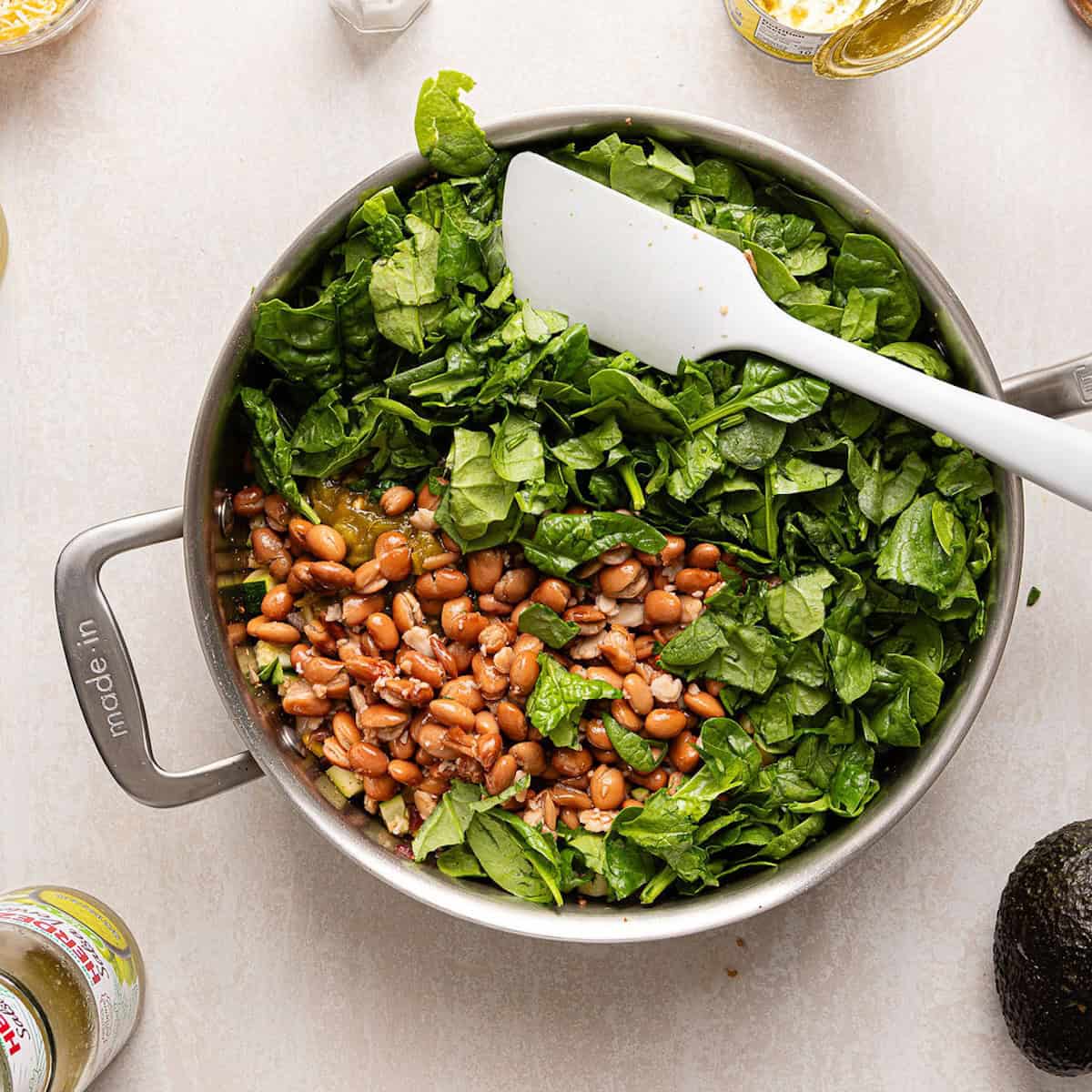 Spinach, pinto beans, and canned green chiles added to a skillet with vegetables.