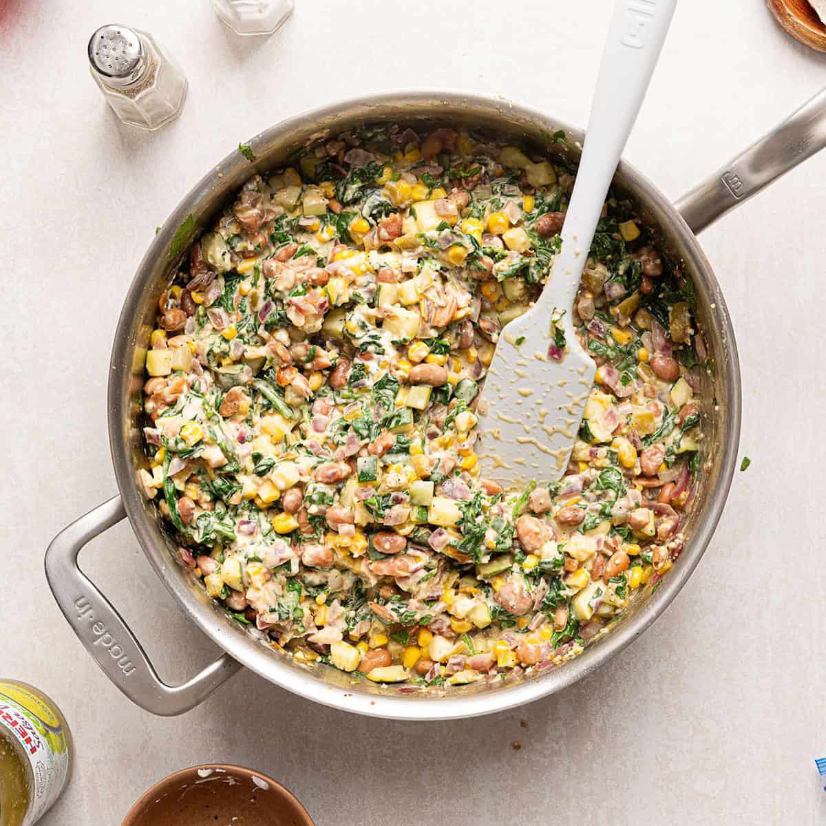 Cheesy vegetarian enchilada recipe filling cooked down in a large skillet with a spatula.