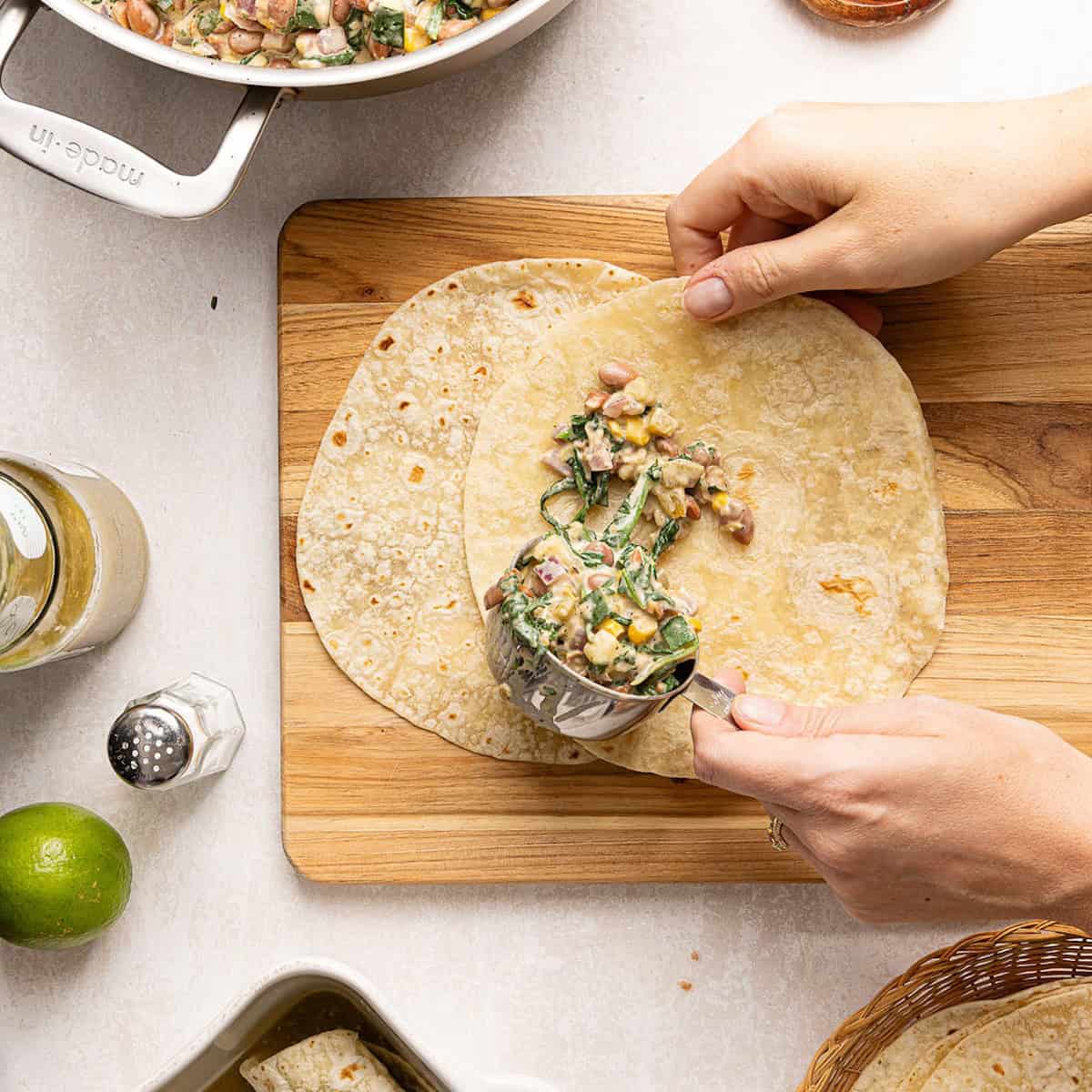 Woman spooning enchilada filling onto a flour tortilla on a cutting board.