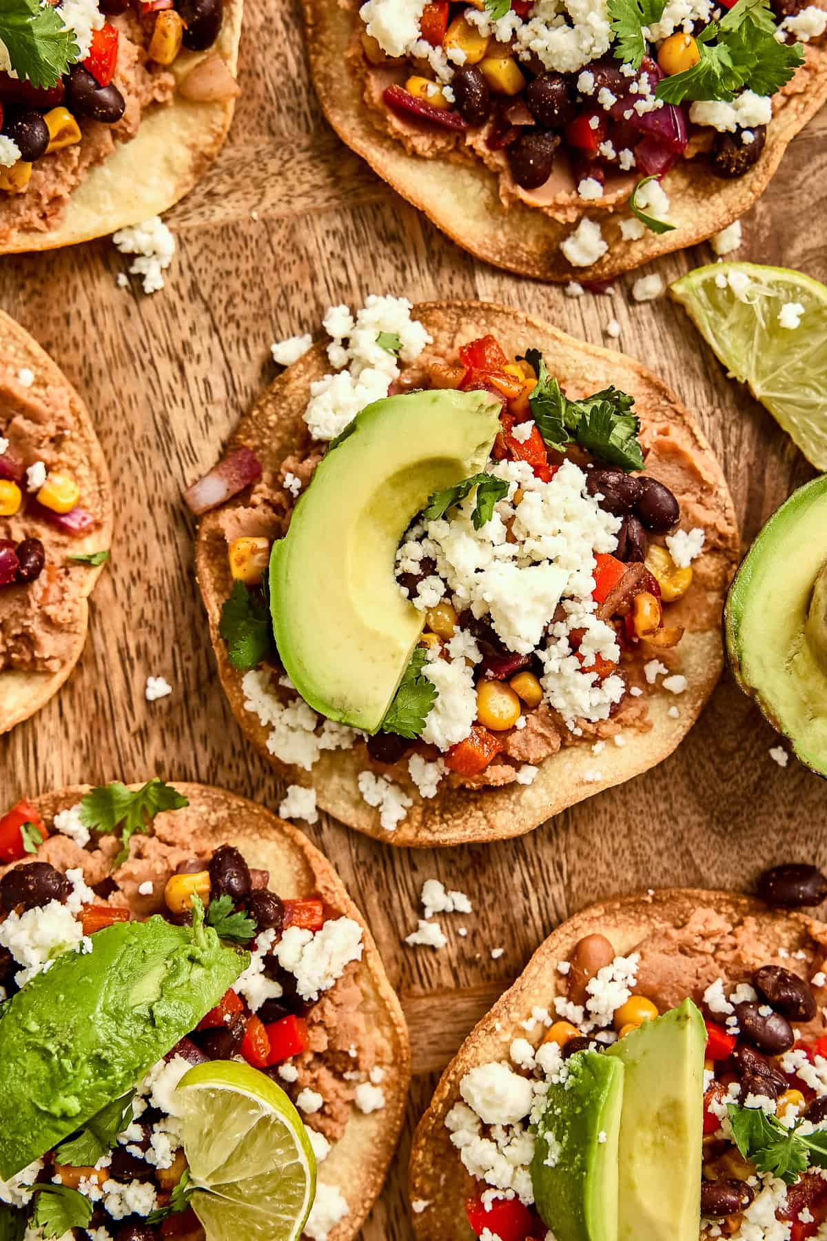 Vegetarian tostadas topped with avocado slices and lime wedges on a wooden board.