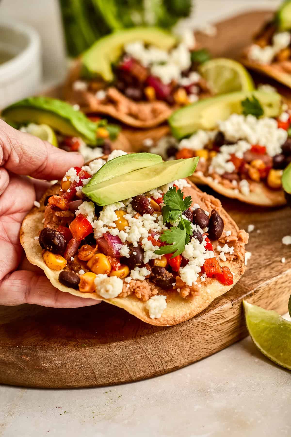 Woman holding a veggie tostada with cheese and avocado in her hand.