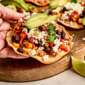 Woman holding a veggie tostada with cheese and avocado in her hand.