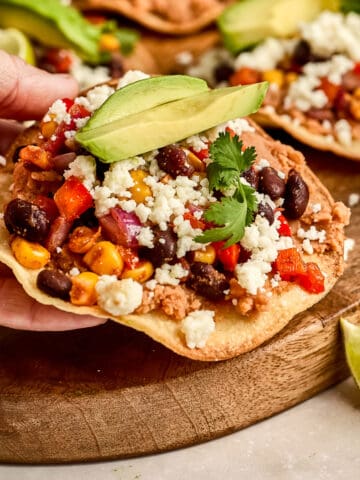 Woman holding a veggie tostada with cheese and avocado in her hand.