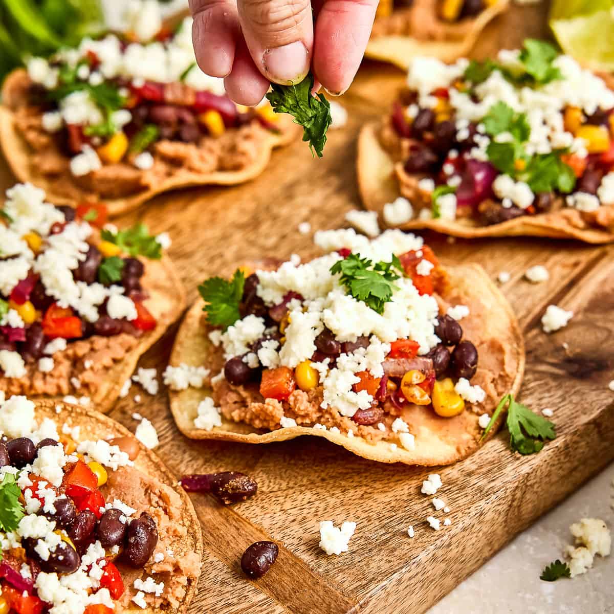 Woman sprinkling chopped cilantro on a tostada next to others on a board.