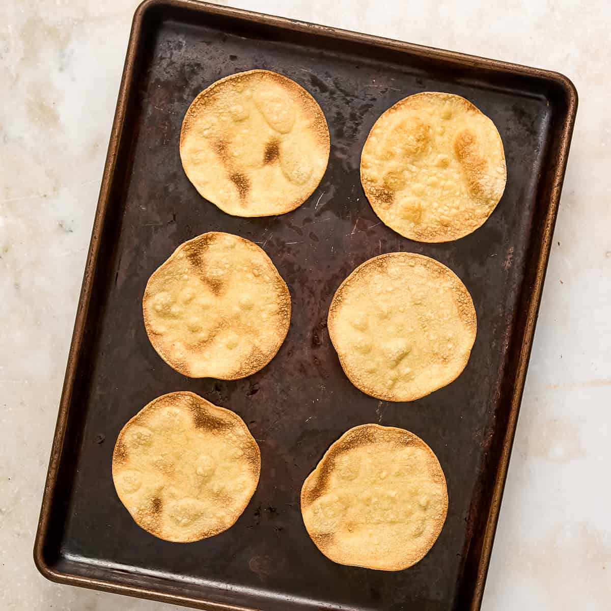 Crispy corn tortillas on a baking sheet after coming out of the oven.