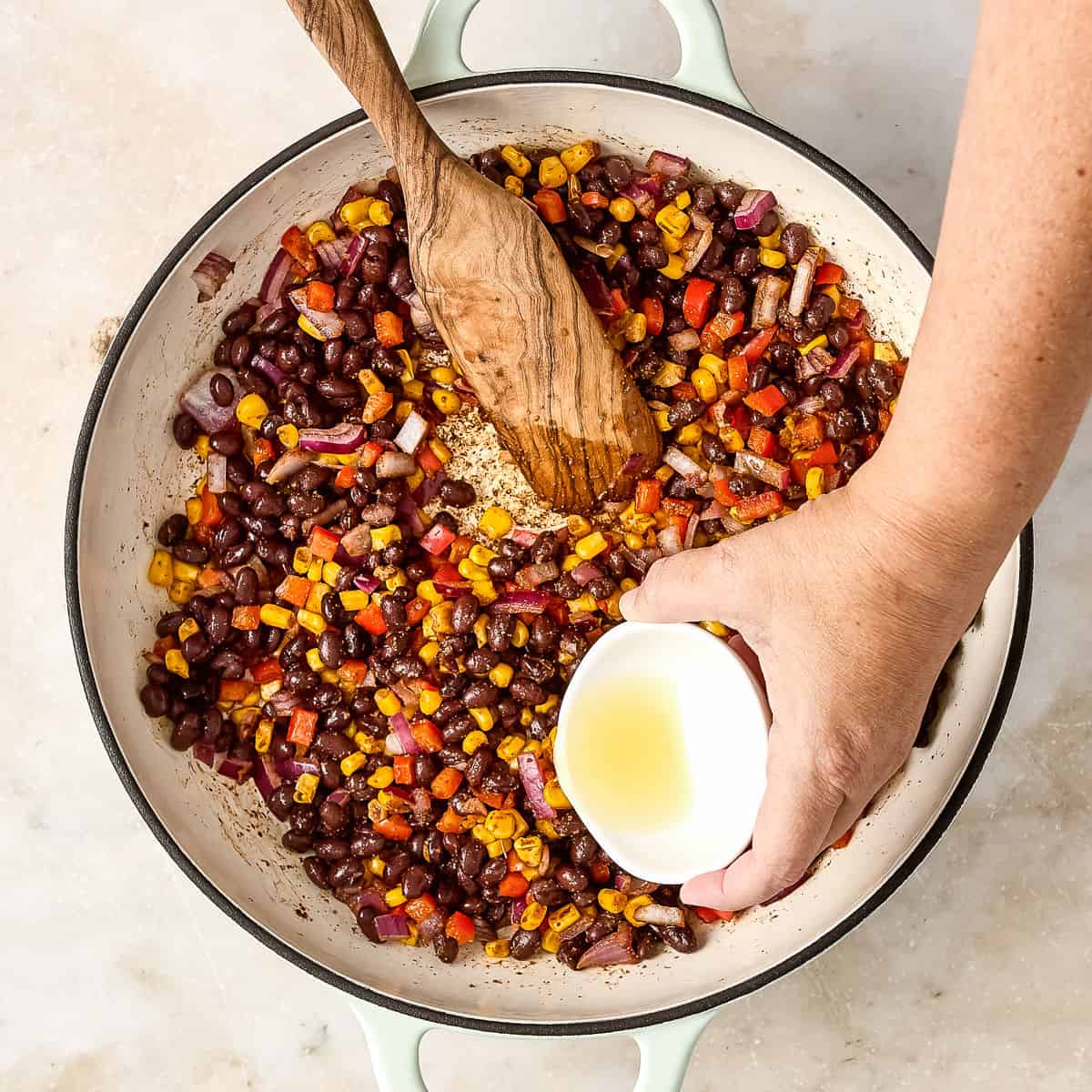 Woman pouring lime juice into a skillet of cooked vegetables and black beans.