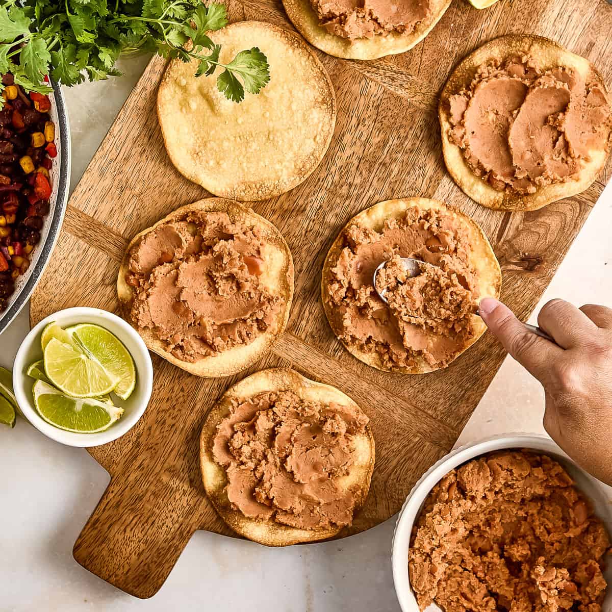 Woman spreading refried beans on crispy tortillas on a board.