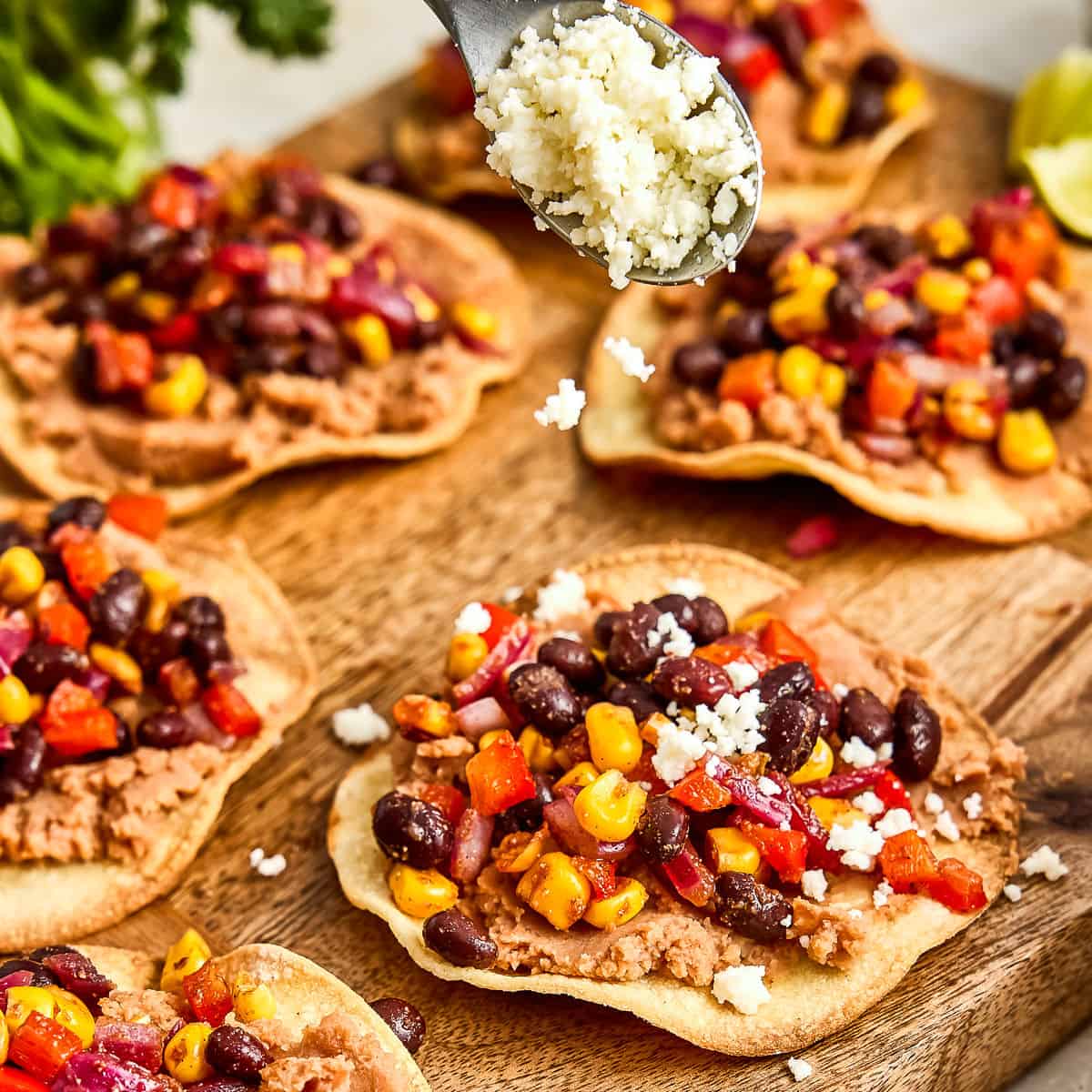 Woman sprinkling cotija cheese on vegetarian tostadas next to others on a board.
