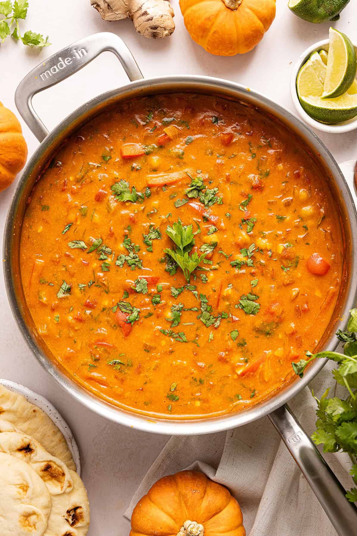 Pumpkin chickpea curry with cilantro in a large skillet surrounded by ingredients.