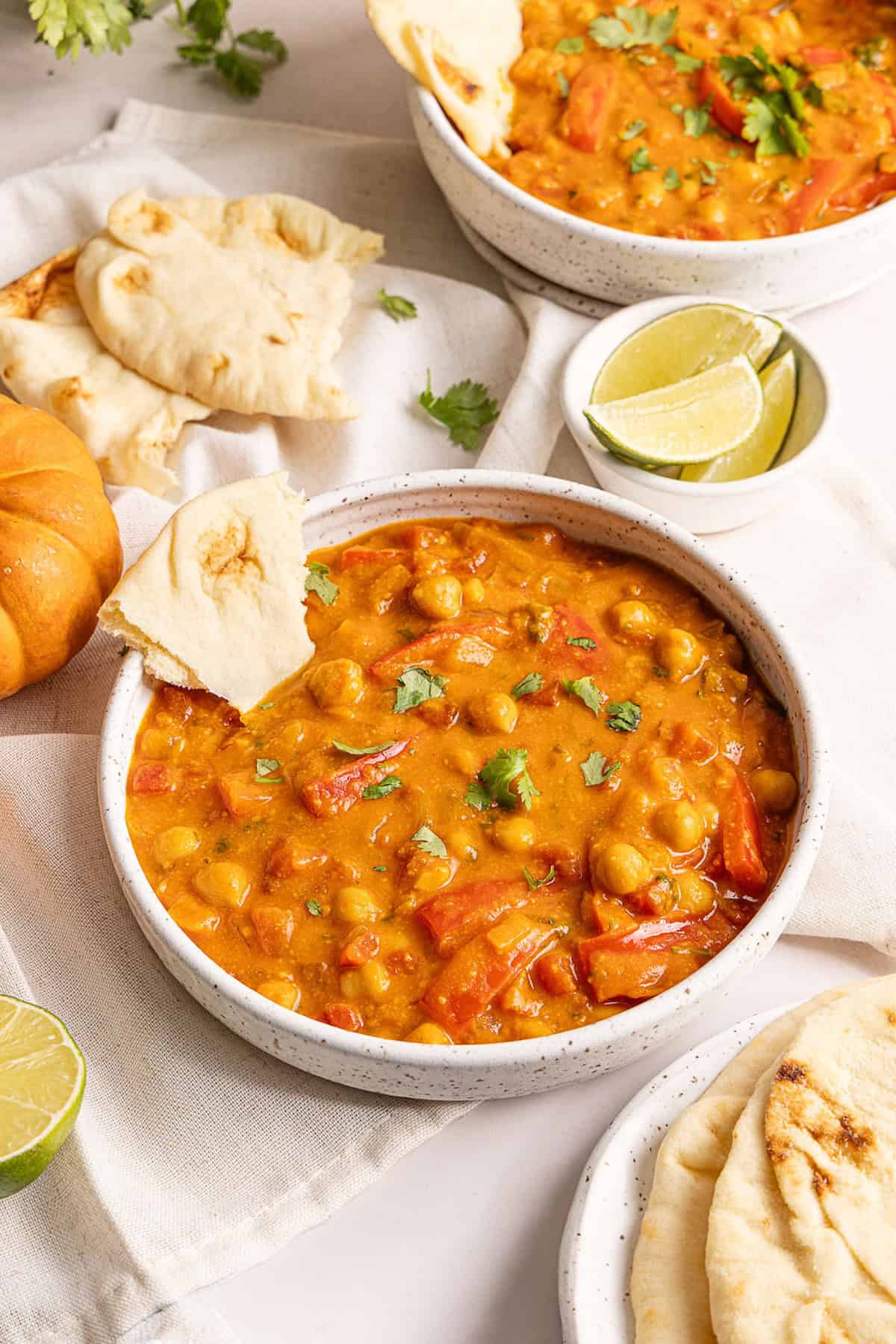 Pumpkin curry with a piece of naan in a bowl next to ingredients and mini pumpkin.