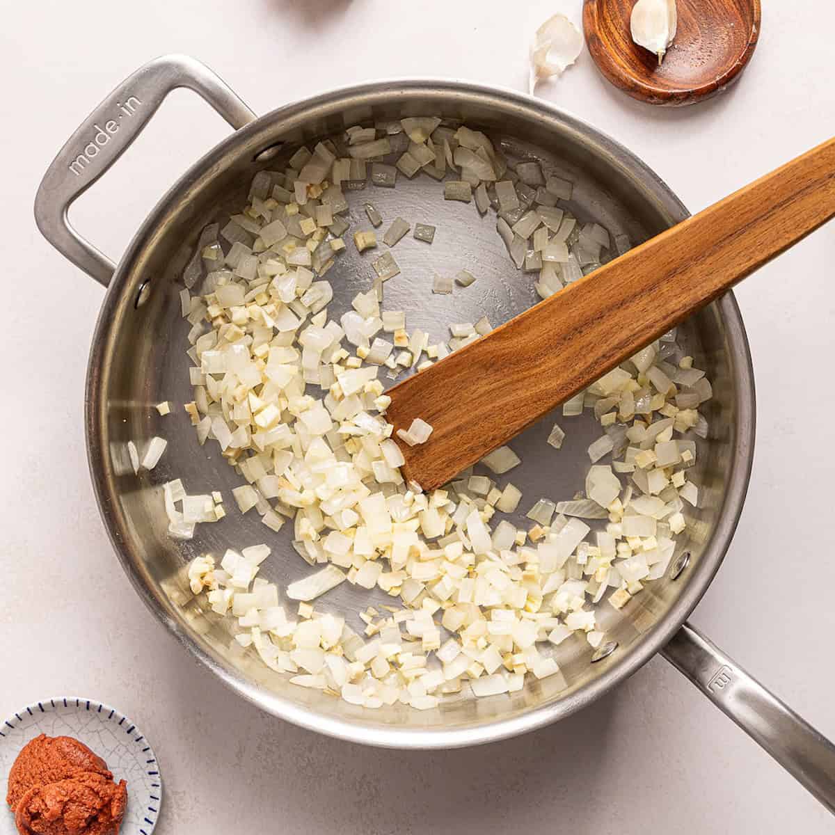 Onions and garlic cooking in olive oil in a large skillet with a wooden spoon.