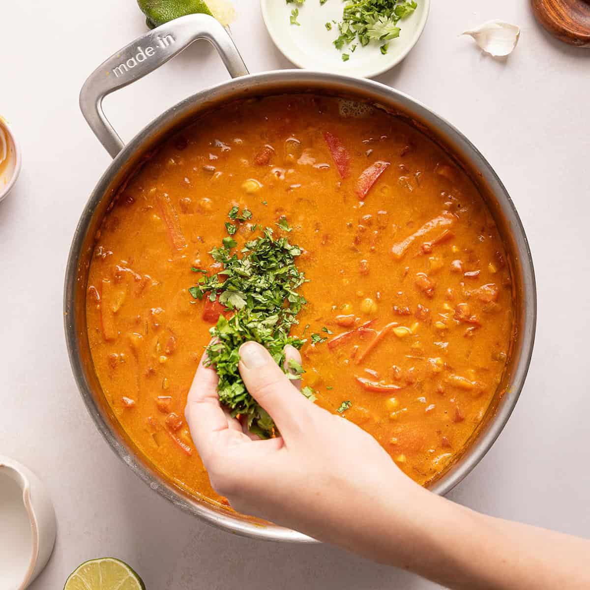 Woman sprinkling chopped cilantro into curry cooking in a skillet.