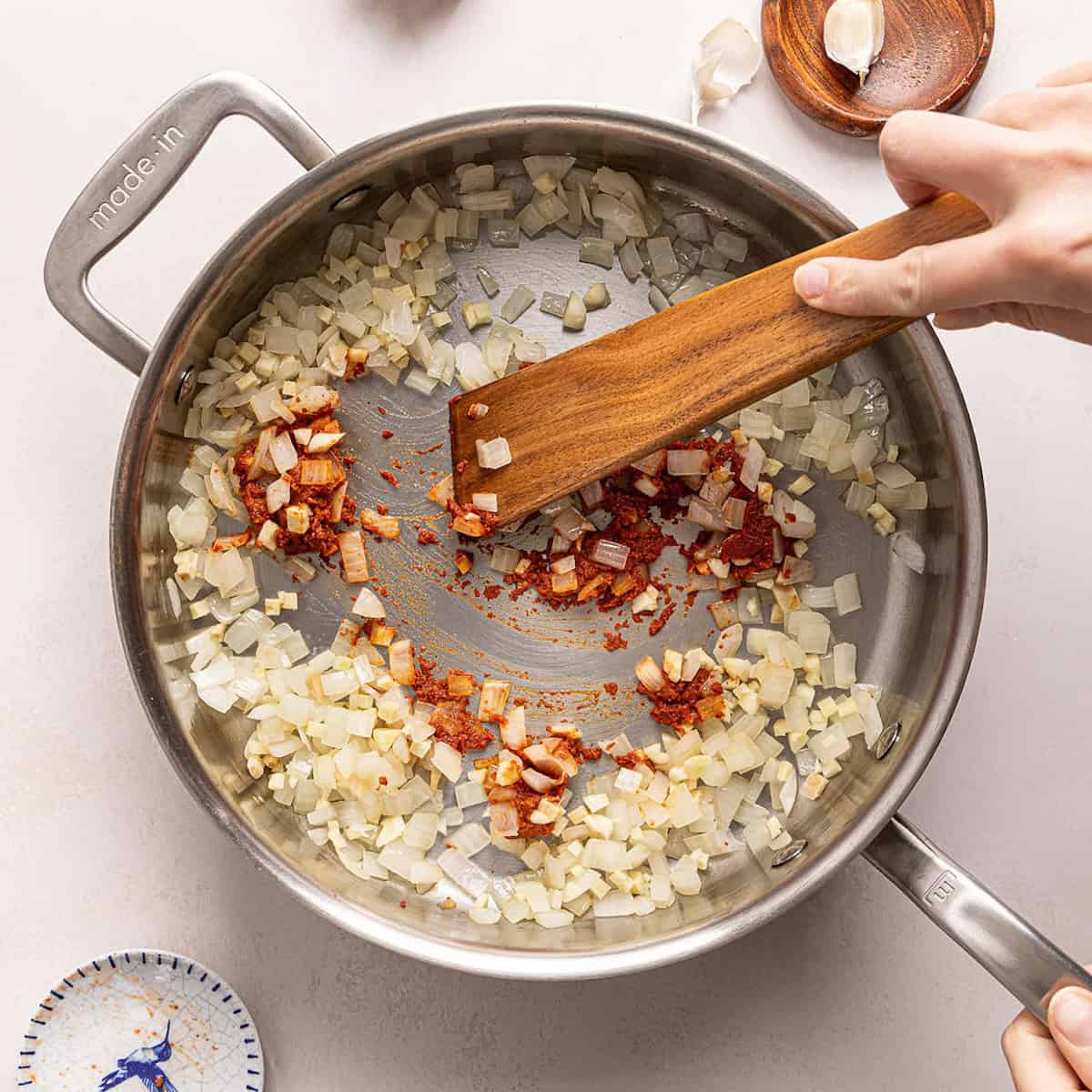 Woman stirring red curry paste into softened onions in a large skillet.