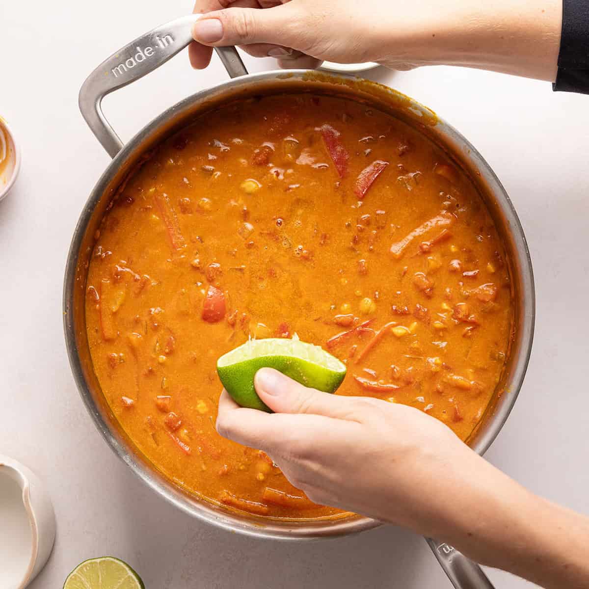 Woman squeezing half of a lime into a skillet of chickpea curry.