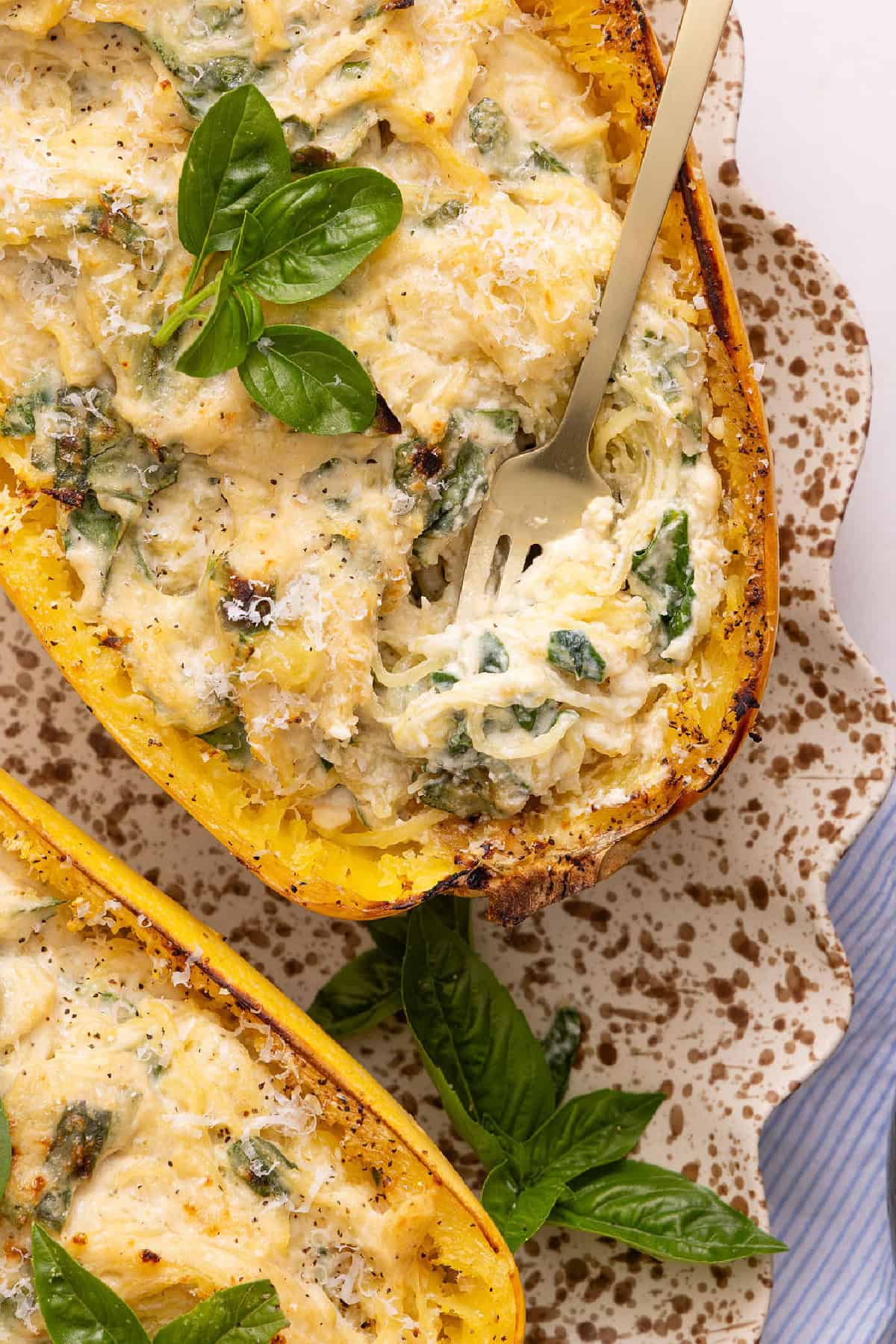 A fork inserted into a spaghetti squash alfredo boat on a serving platter.