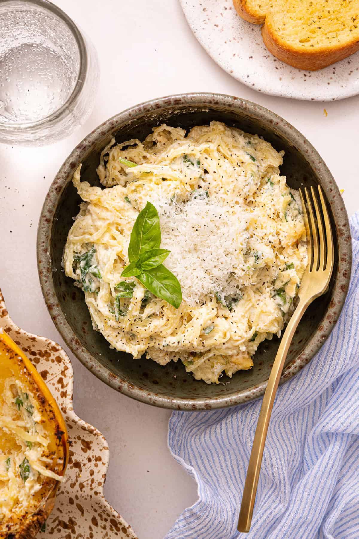Spaghetti squash strands with healthy alfredo sauce in a bowl with a fork, cheese, and basil.