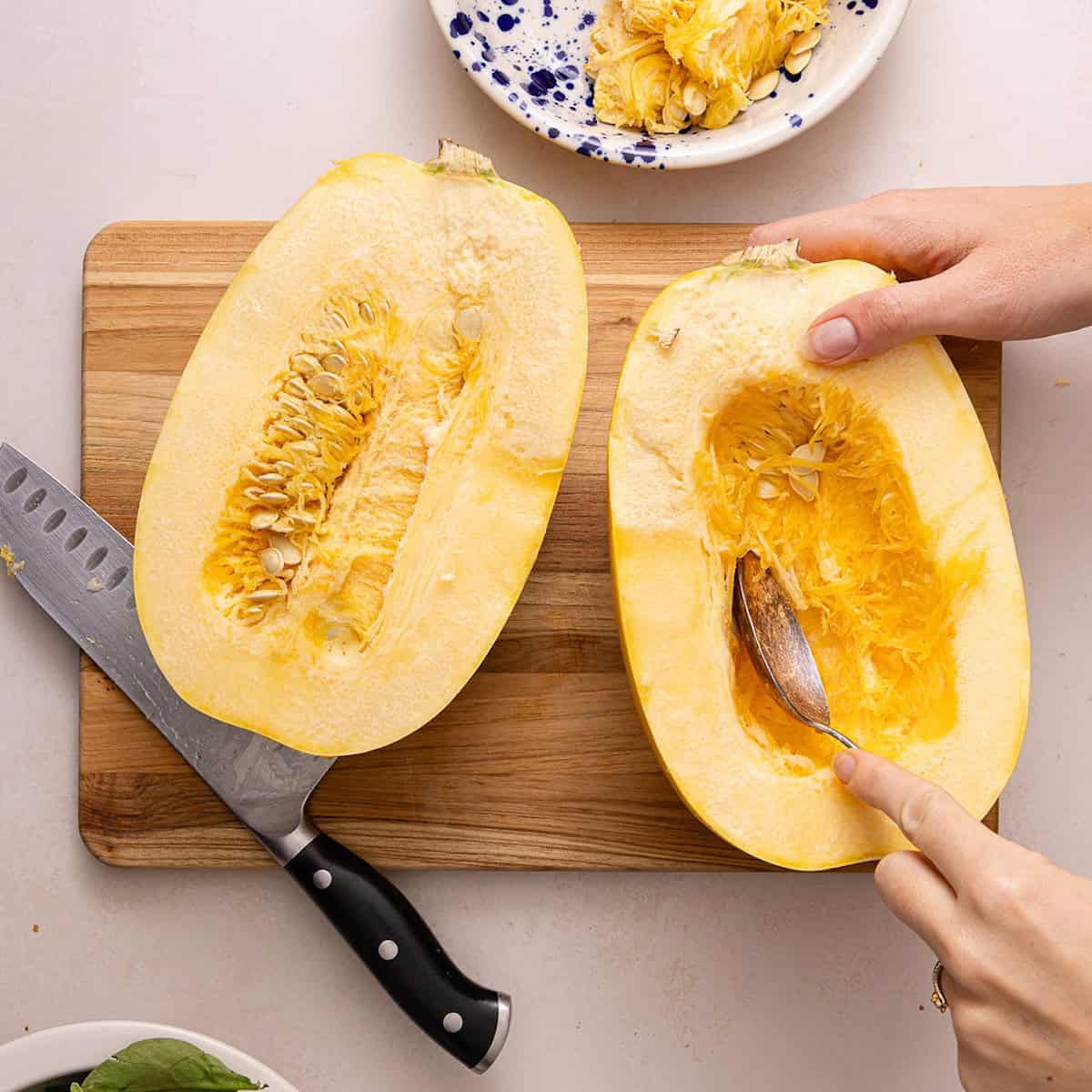 Woman scooping seeds out of half of a spaghetti squash.