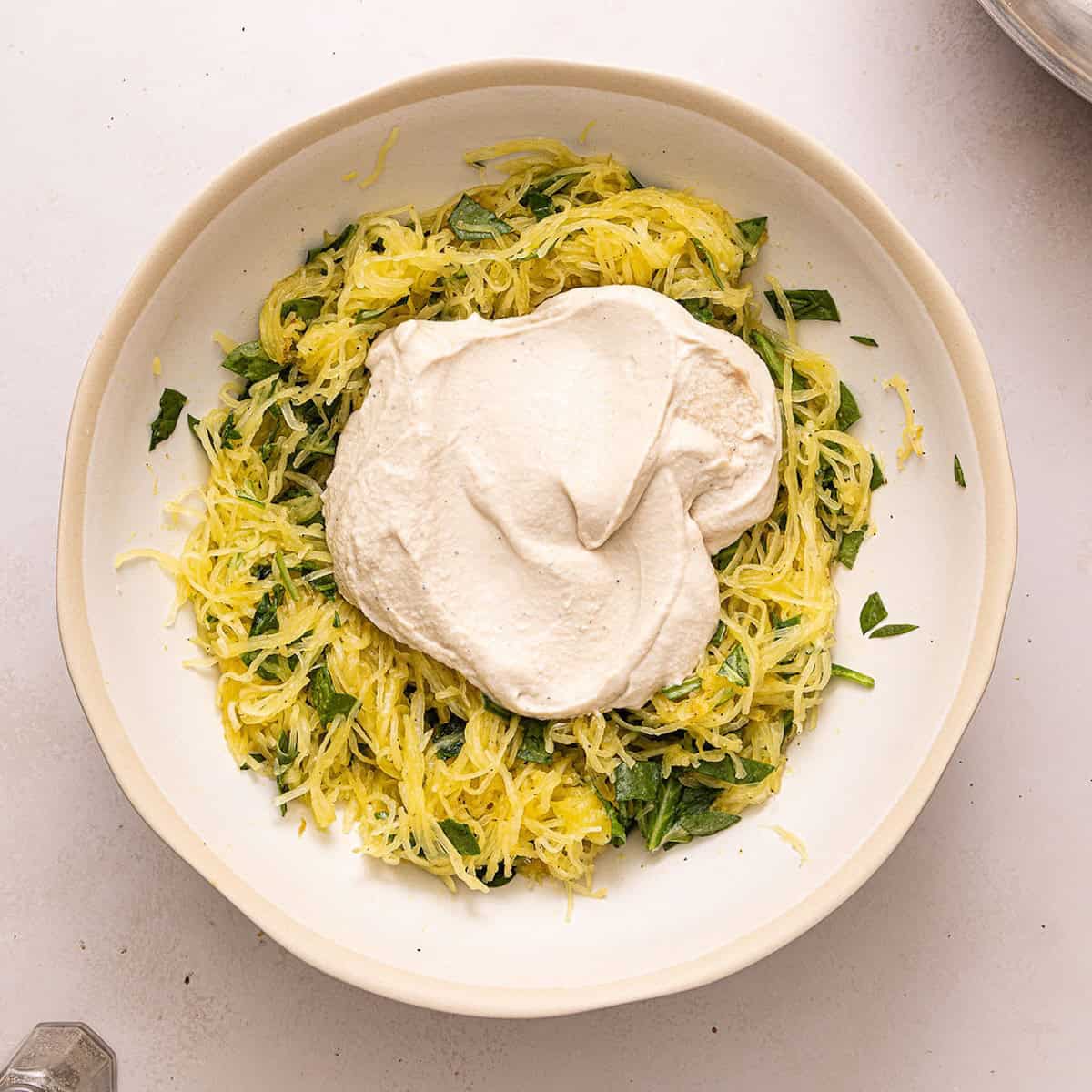 Spaghetti squash and baby spinach with healthy alfredo sauce on top in a bowl.