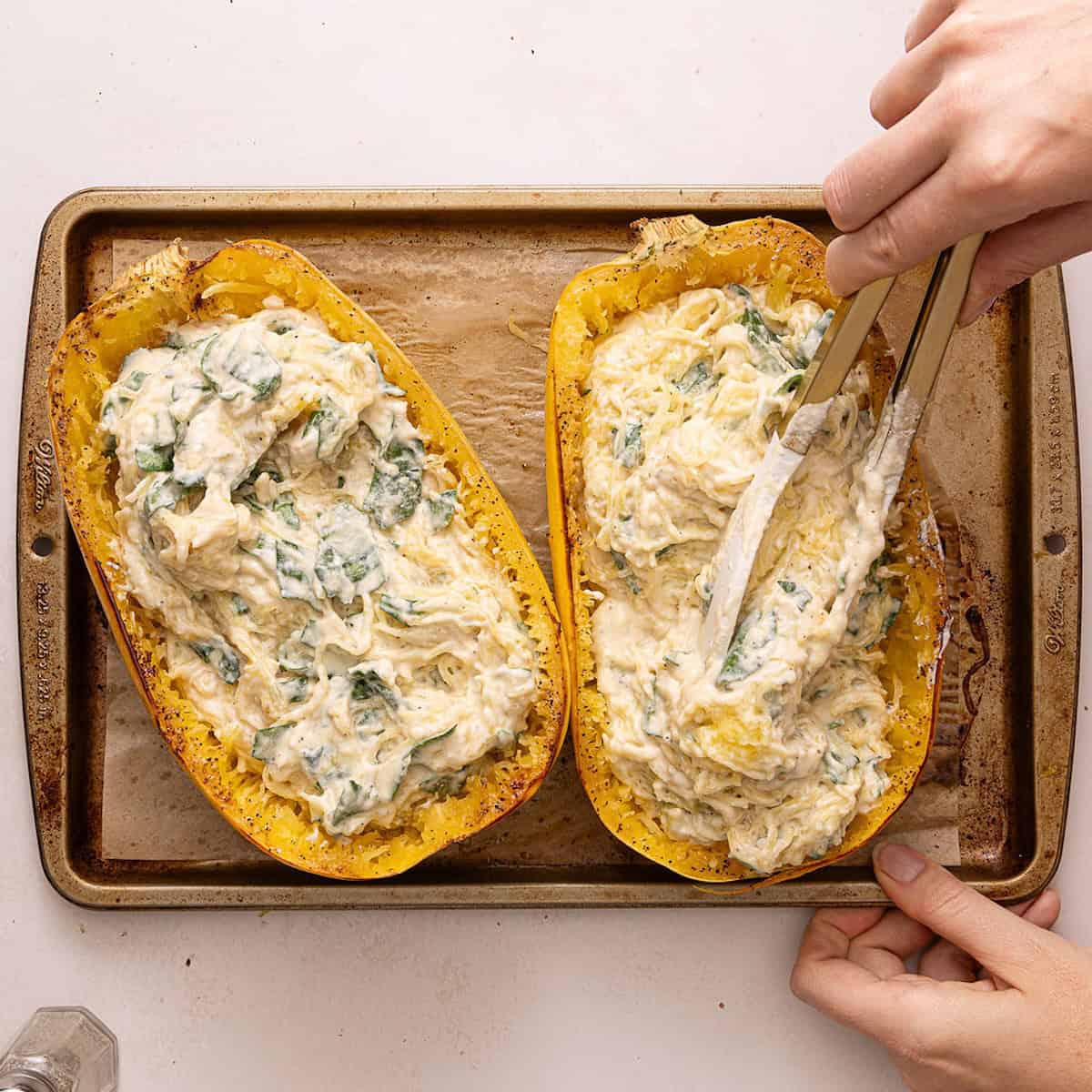 Woman using tongs to put spaghetti squash alfredo back into squash halves.