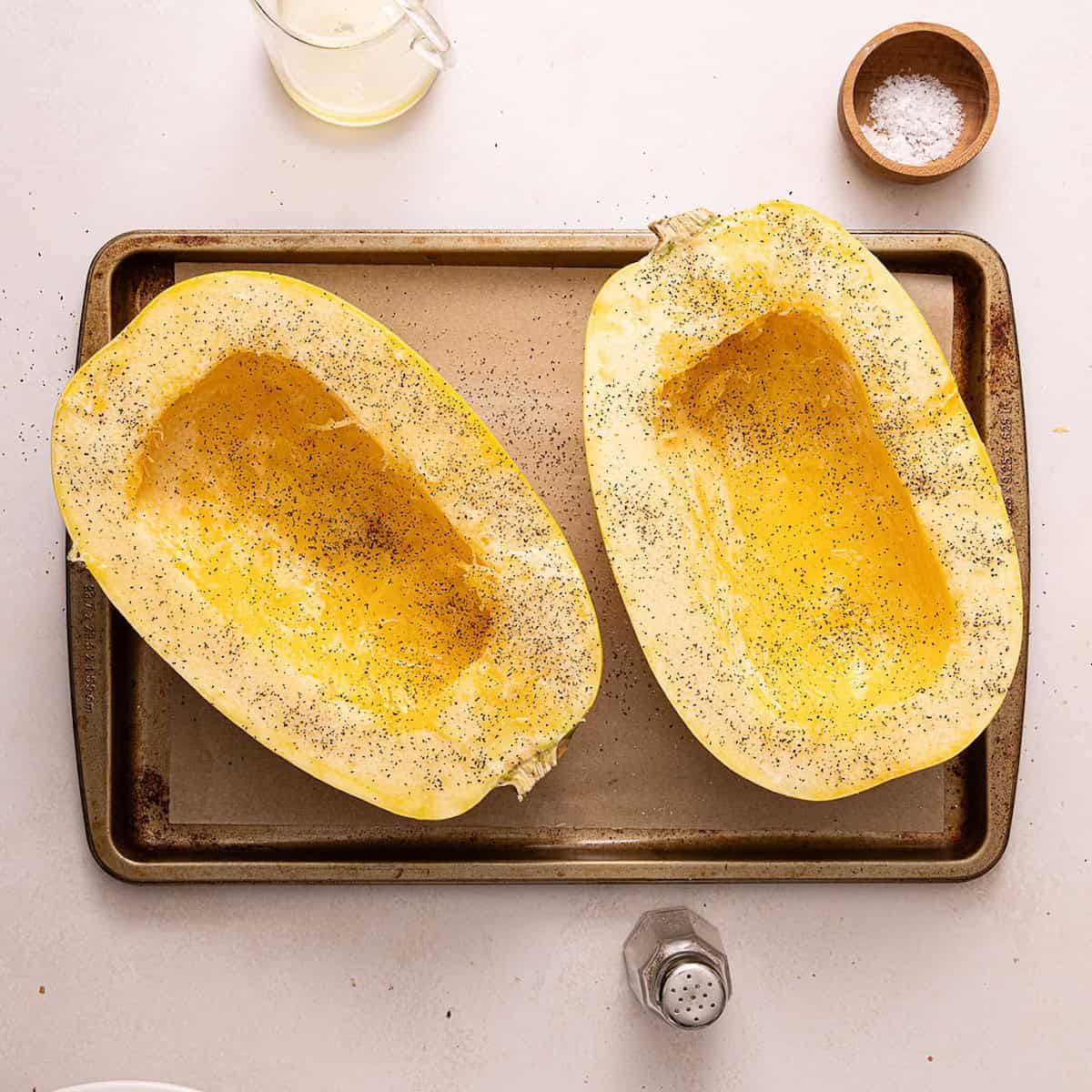 Salt, pepper, and olive oil sprinkled on spaghetti squash halves.