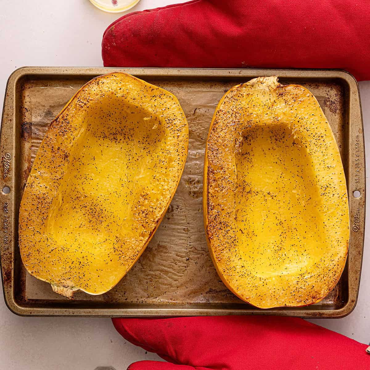 Roasted spaghetti squash halves on a baking sheet after coming out of the oven.