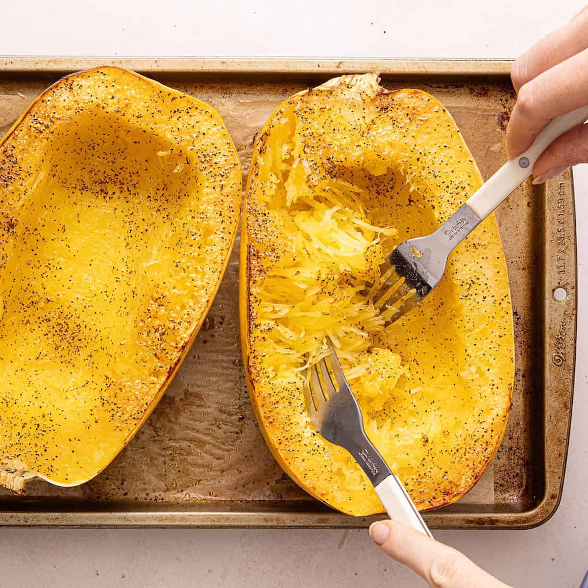 Woman pulling spaghetti squash strands away from the skin with two forks.