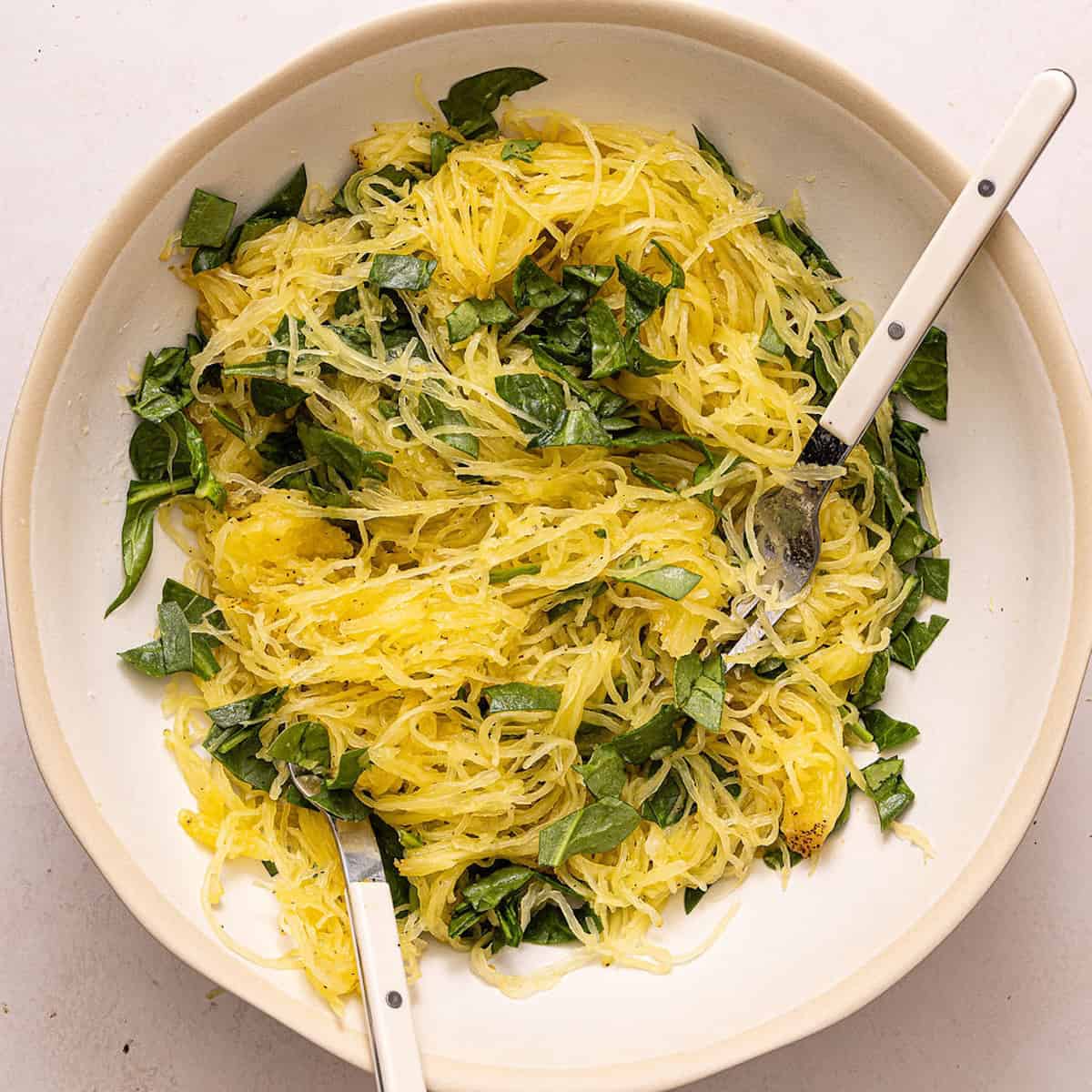Cooked spaghetti squash mixed with chopped baby spinach in a bowl.