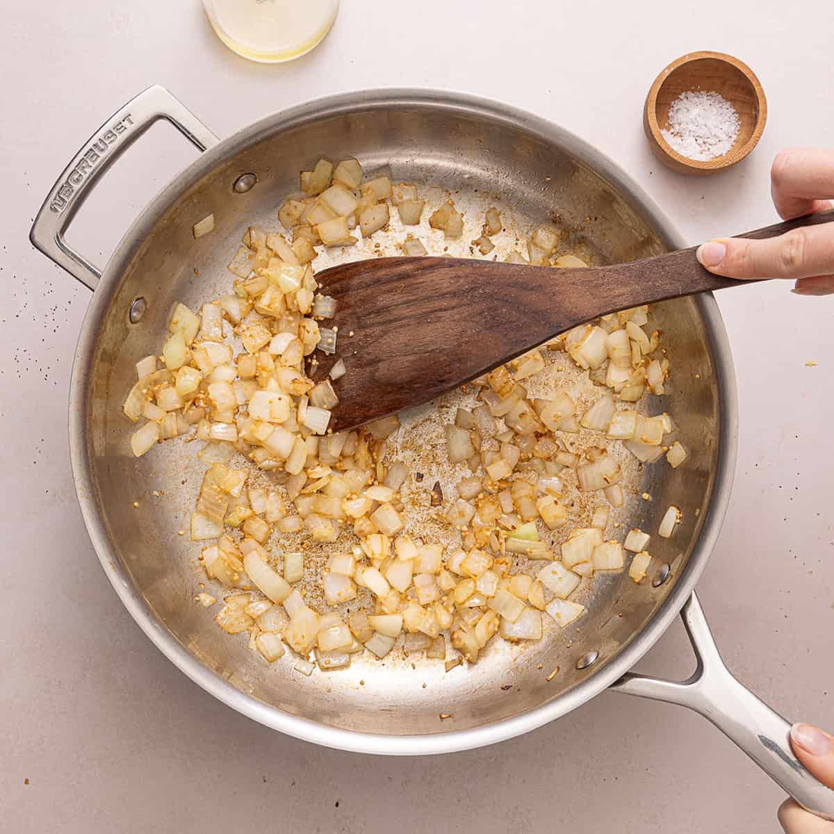 Woman stirring onion and garlic cooking in a skillet.