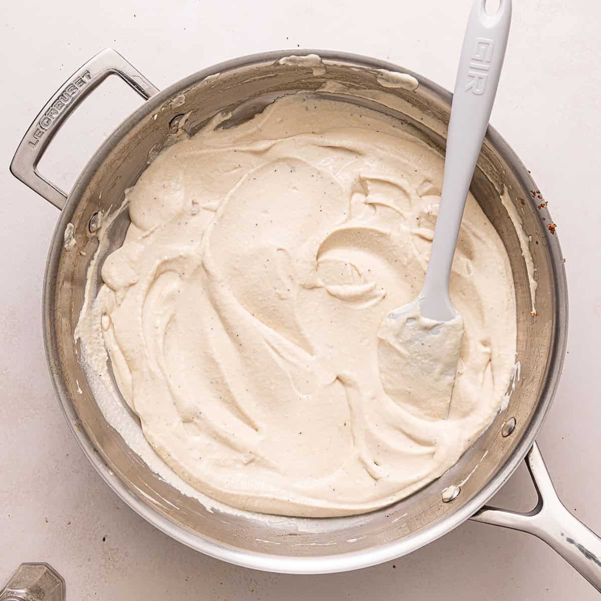 Healthy alfredo sauce spread in a skillet with a spatula.